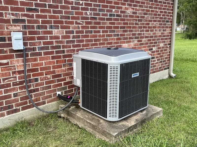 A new S&S installed outdoor AC unit on a fresh pad against a red brick wall