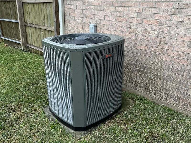 An S&S serviced outdoor AC unit on its pad beside a brick home and a wood fence