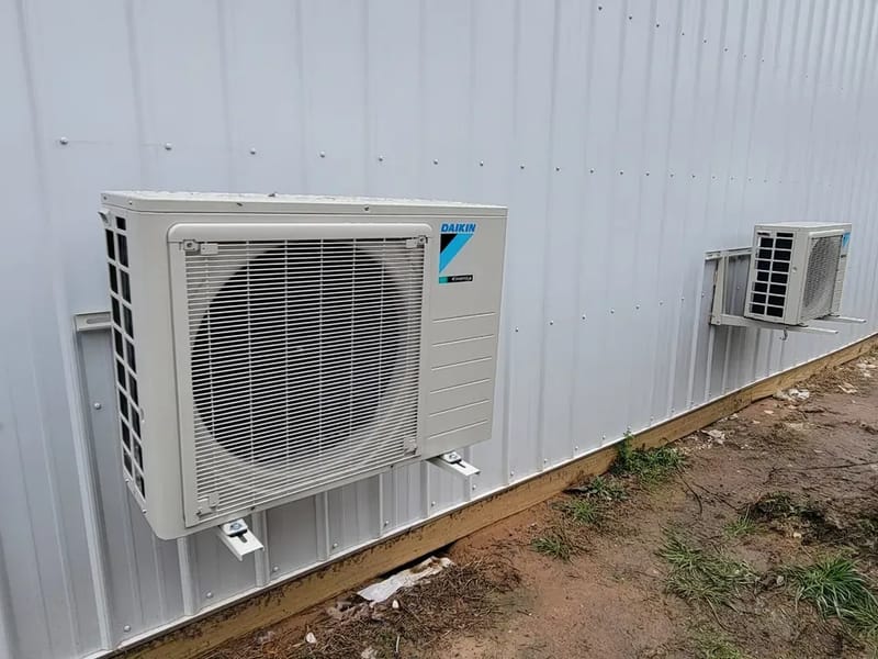 An outdoor ductless mini-split unit mounted on the metal wall of a shop building
