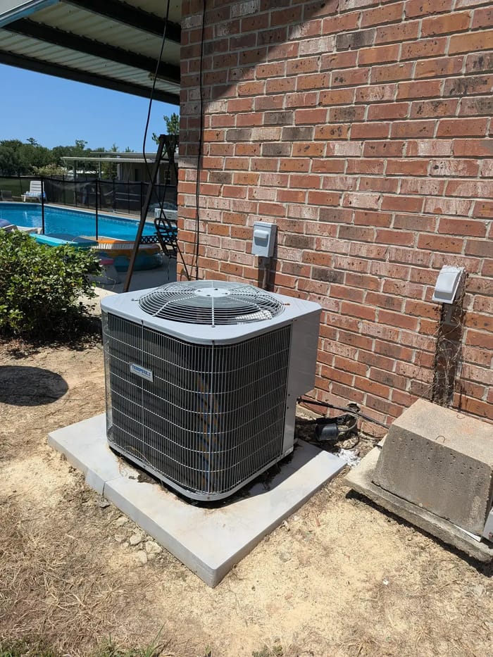 A new outdoor AC unit on a fresh concrete pad beside a brick home and a pool