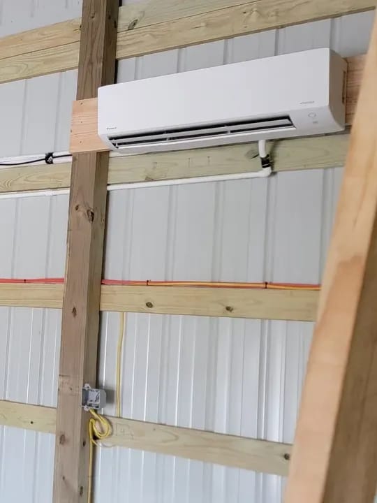 A ductless mini-split head mounted high on the wall of a shop with the line set run along the framing