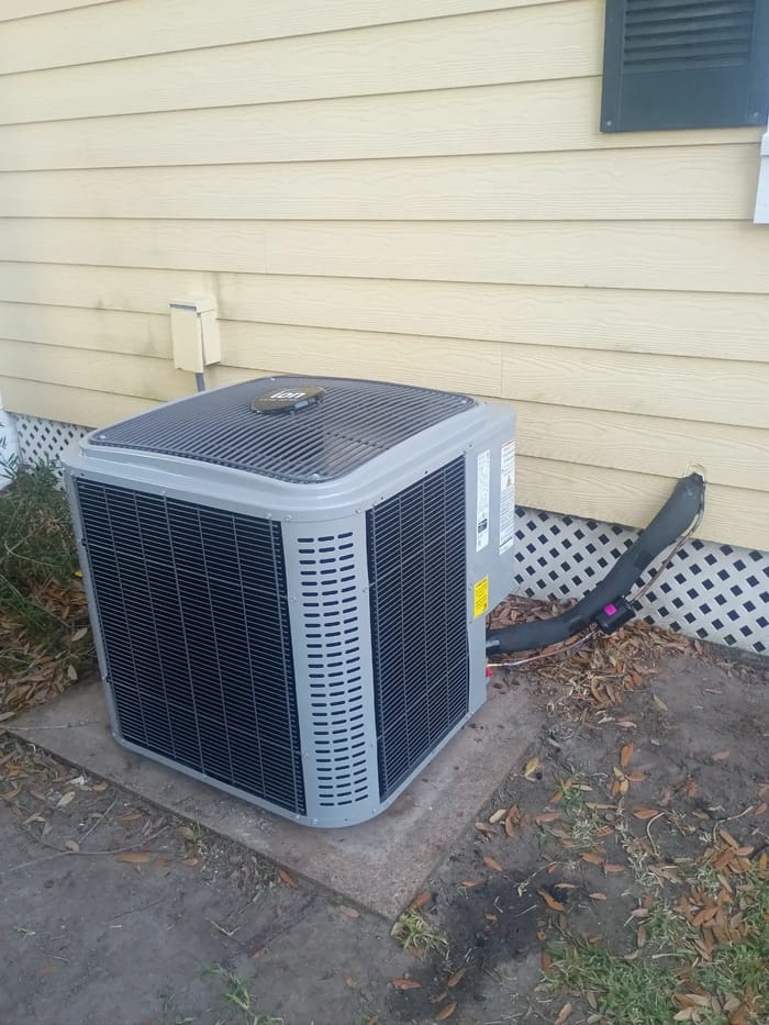 A new outdoor AC unit on its pad beside a home with yellow siding